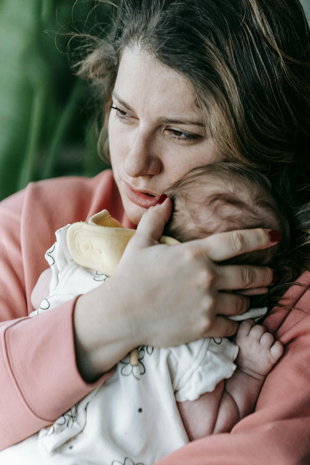 A sad woman lost in thought while holding her baby close | Source: Pexels