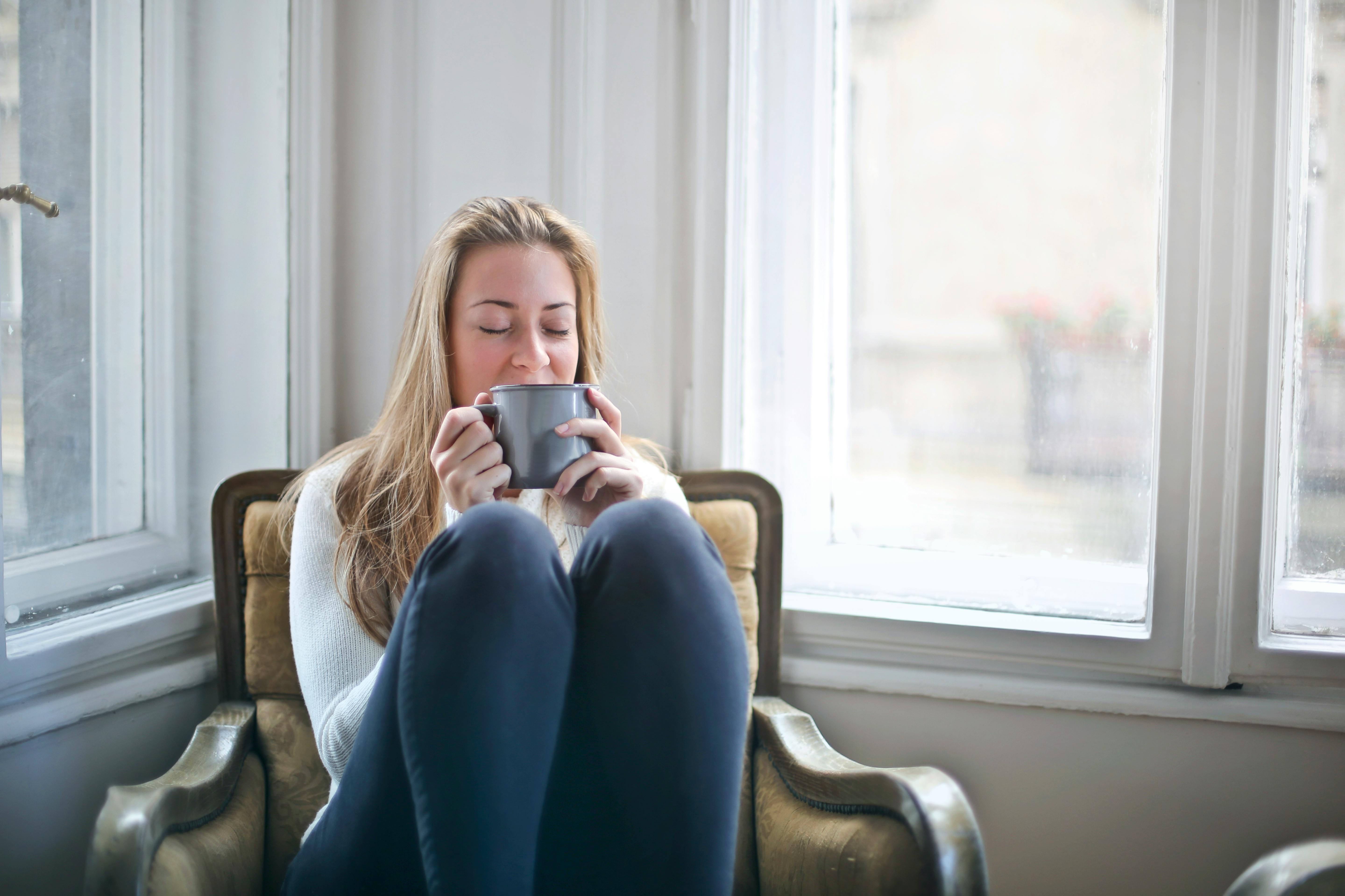 Woman sitting by a window and drinking from a mug | Source: Pexels
